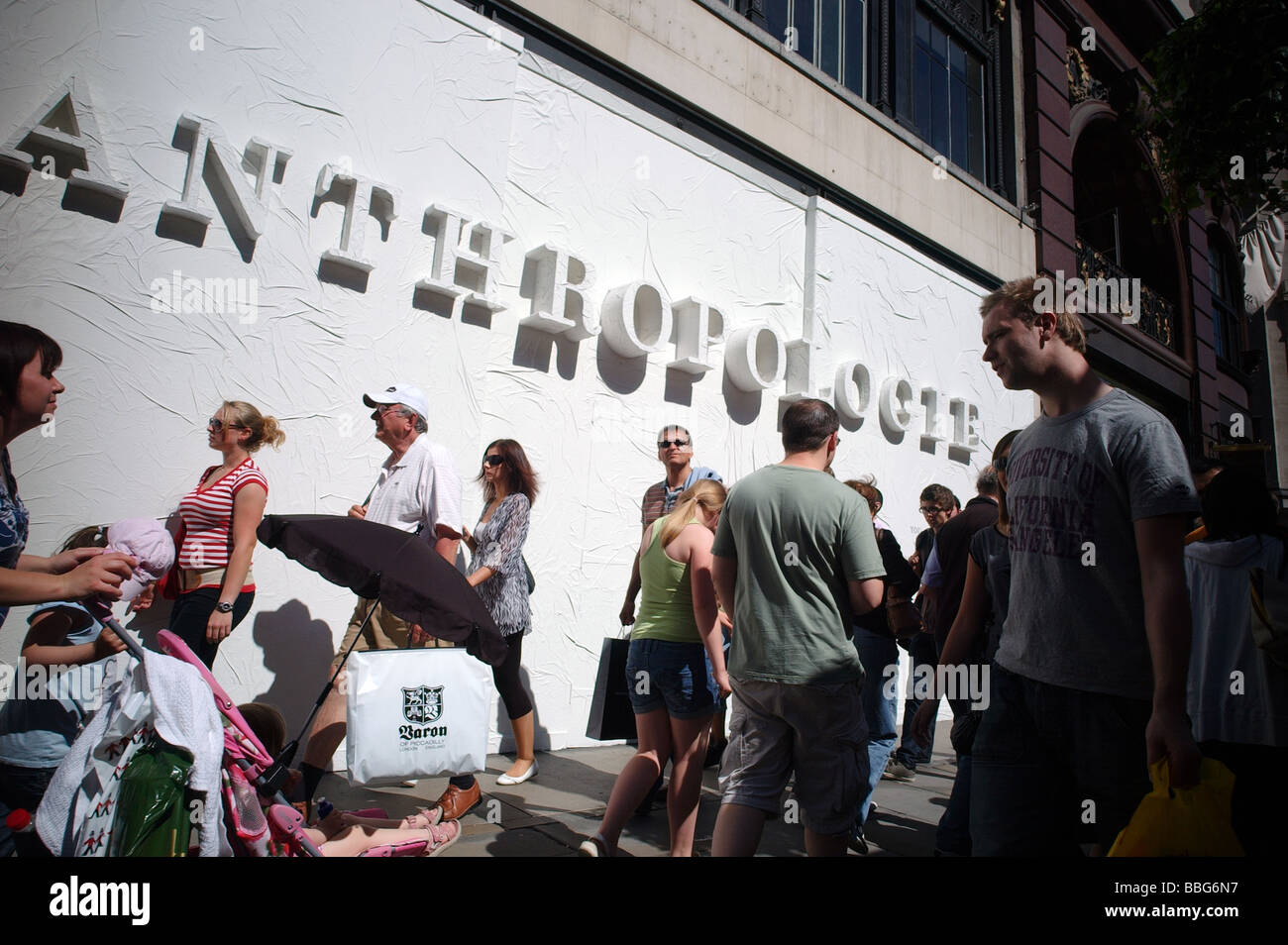 A crowd of people walking past a bill board for Anthropologie a new shop shortly opening in exclusive Regents  London UK Stock Photo