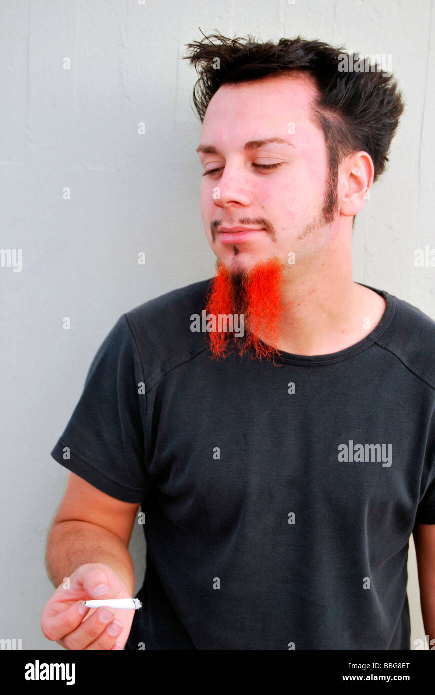 Drugs, young man with red-black beard holding a joint, hand-rolled cigarette Stock Photo