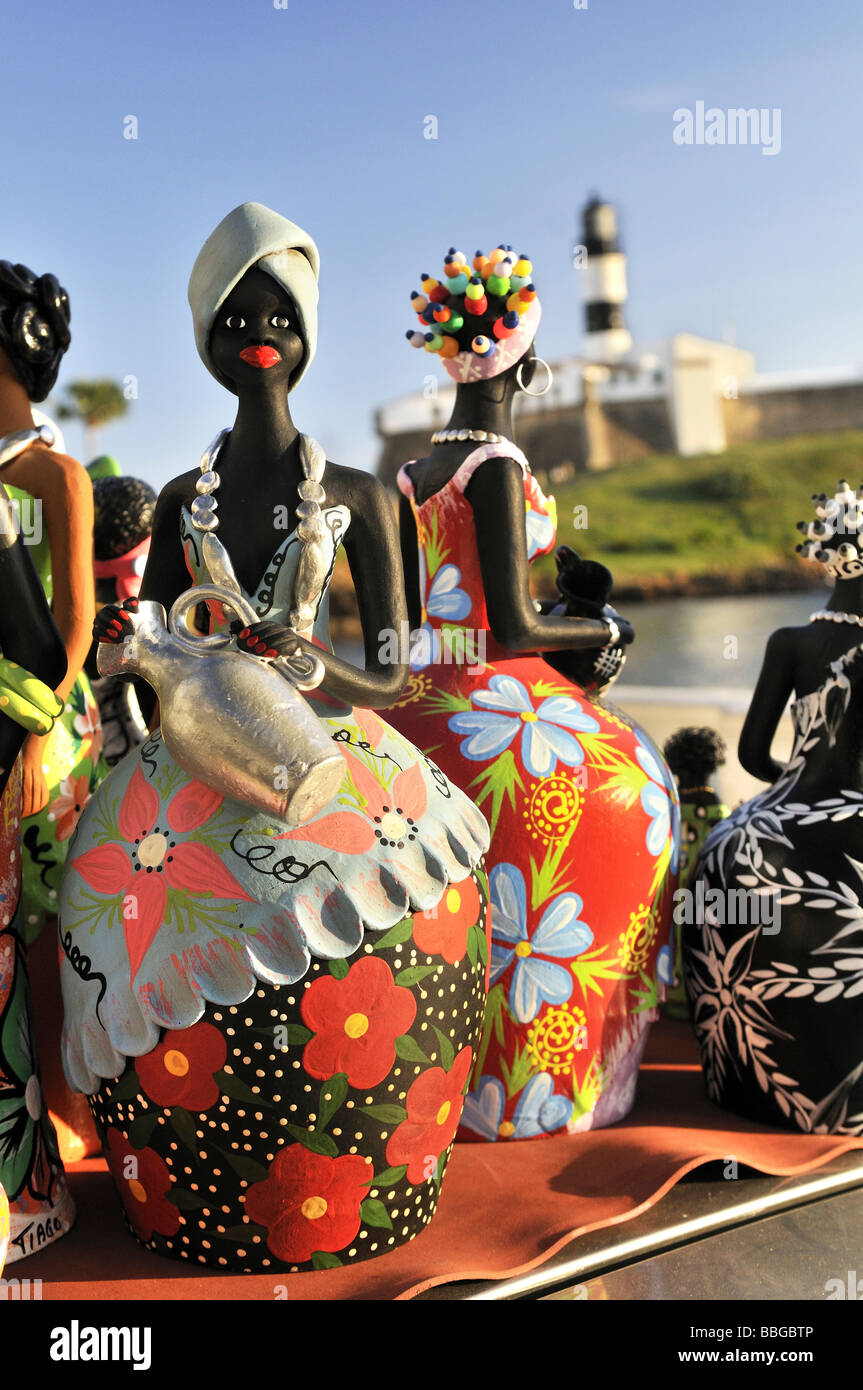 Traditional arts and crafts, clay figurines of women, and Forte de Santo Antonio da Barra fortress with Farol da Barra lighthou Stock Photo