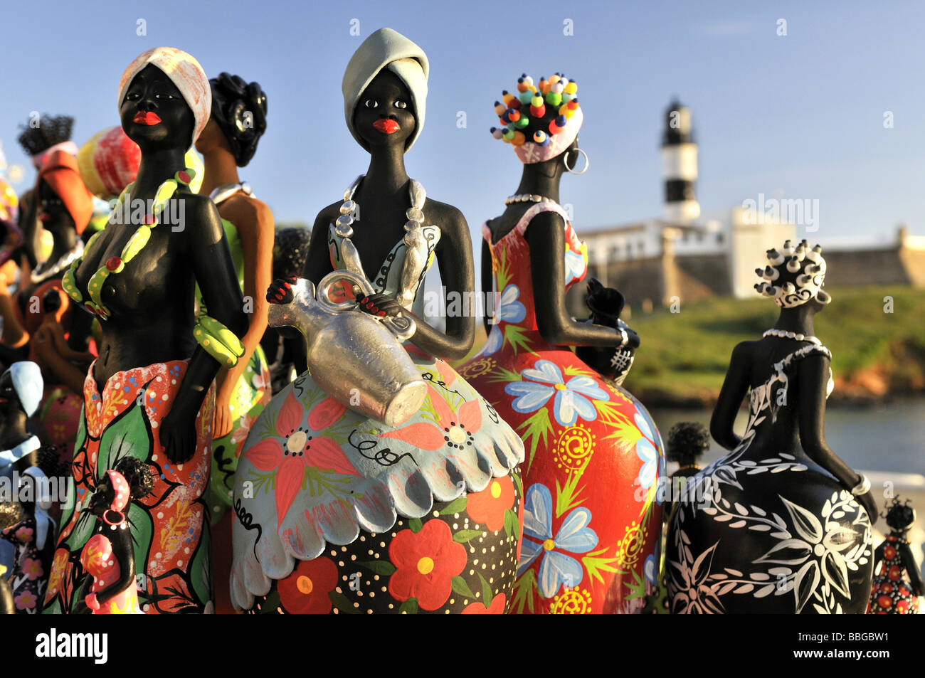 Traditional arts and crafts, clay figurines of women, and Forte de Santo Antonio da Barra fortress with Farol da Barra lighthou Stock Photo