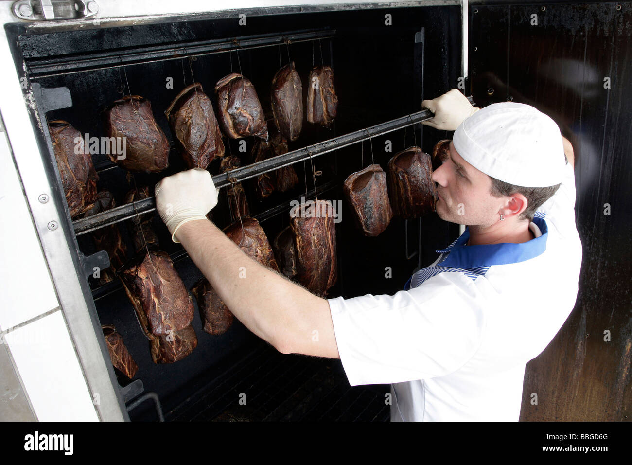 Butcher Gerhard Mader is removing pork joints from a smoker, production of the bavarian specialty Schwarzgeraeuchertes, smoked  Stock Photo