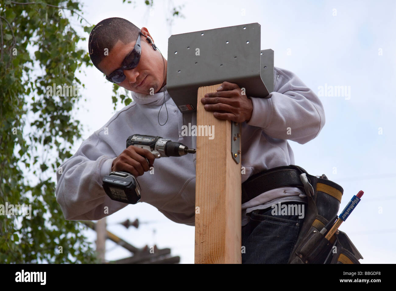 Carpenter using an impact driver to attach a bracket to a post with bolts Stock Photo