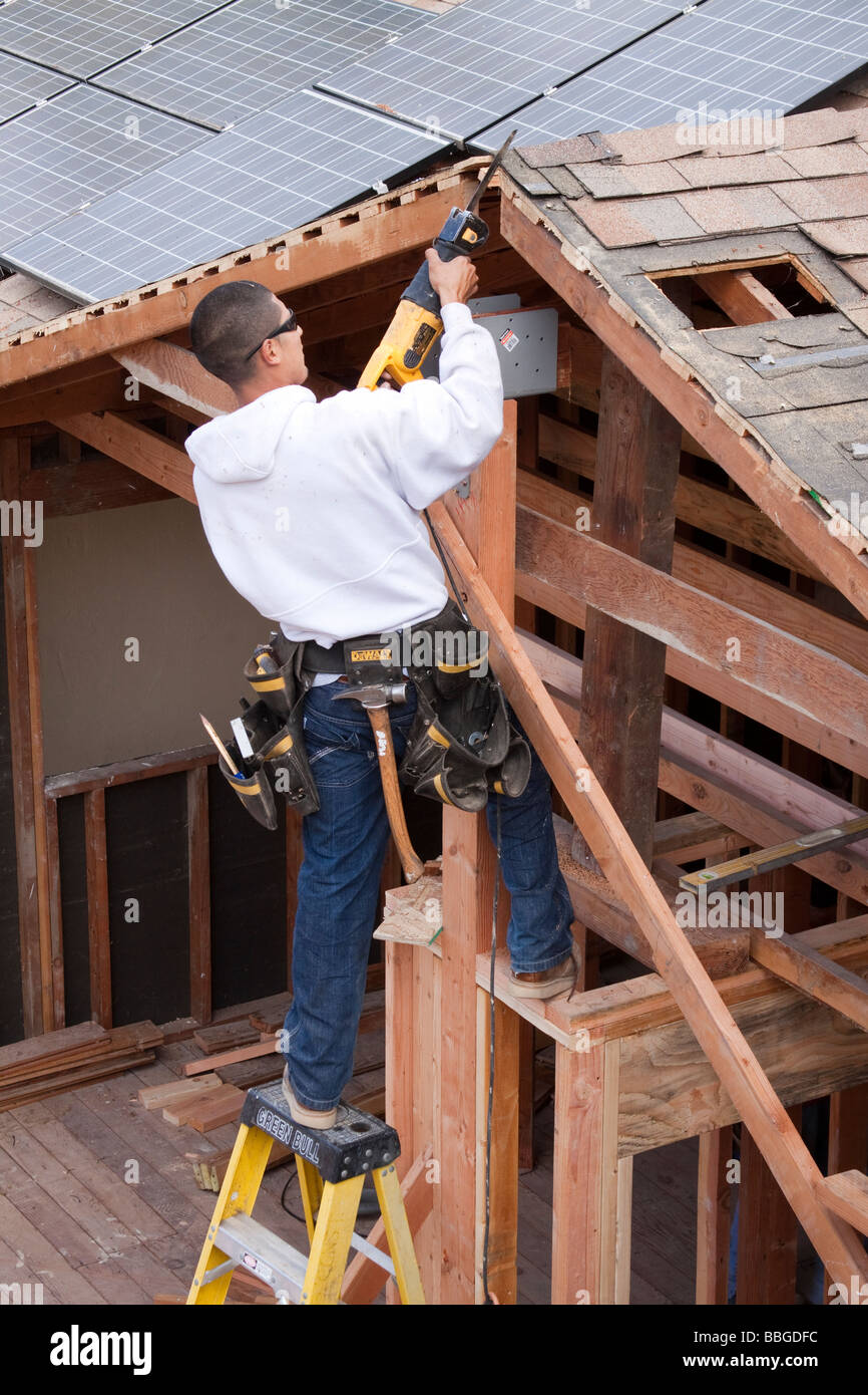 Carpenter standing on ladder and cutting into roof lumber with reciprocating saw Stock Photo
