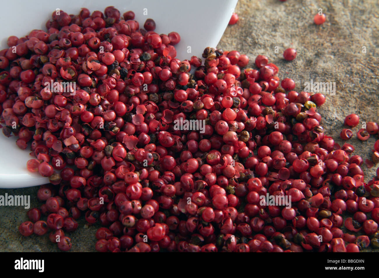 Red peppercorns tipped from a bowl Stock Photo