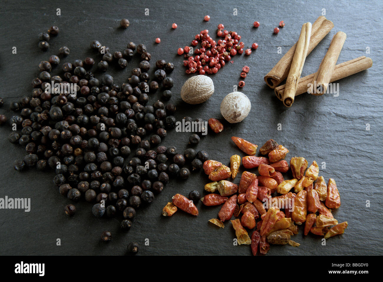 Different spices on a slate, juniper, chili peppers, red pepper, nutmeg, cinnamon sticks Stock Photo