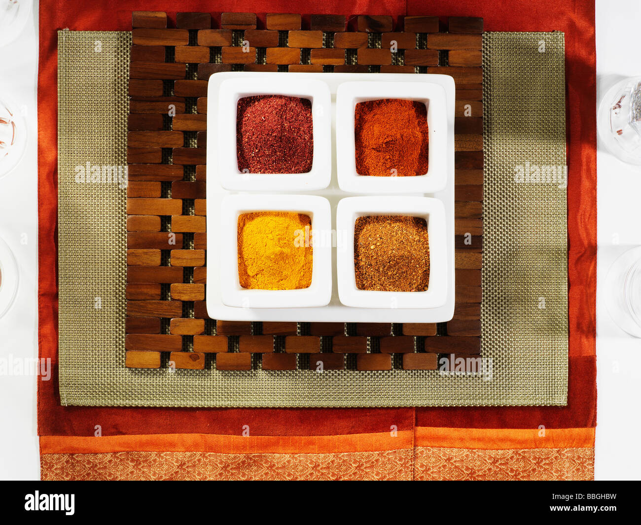 A selection of different spices in a white spice box on a wooden placemat and red background Stock Photo