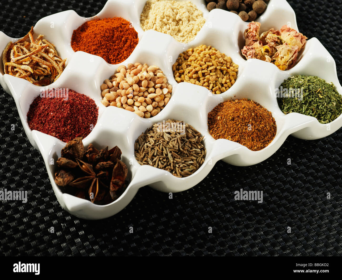 A white pallette of many different spices and seasonings used for cooking shot against a black textured background Stock Photo