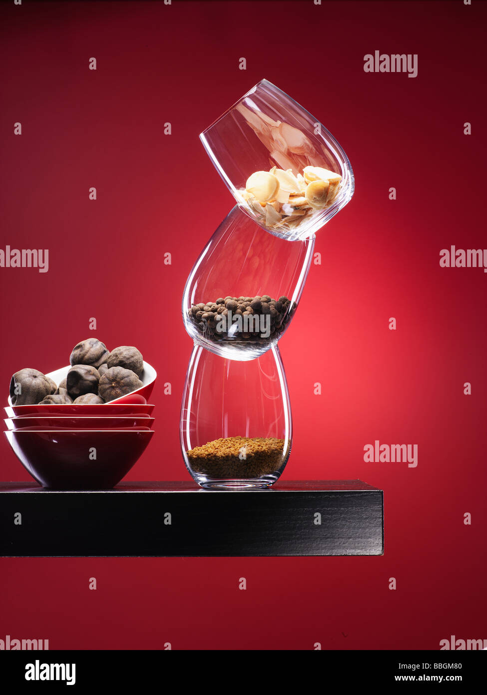 Spices in glass on walnut wooden shelf with deep red spotlit background Stock Photo