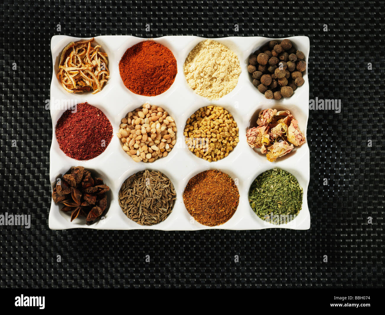 A white pallette of many different spices and seasonings used for cooking shot against a black textured background Stock Photo
