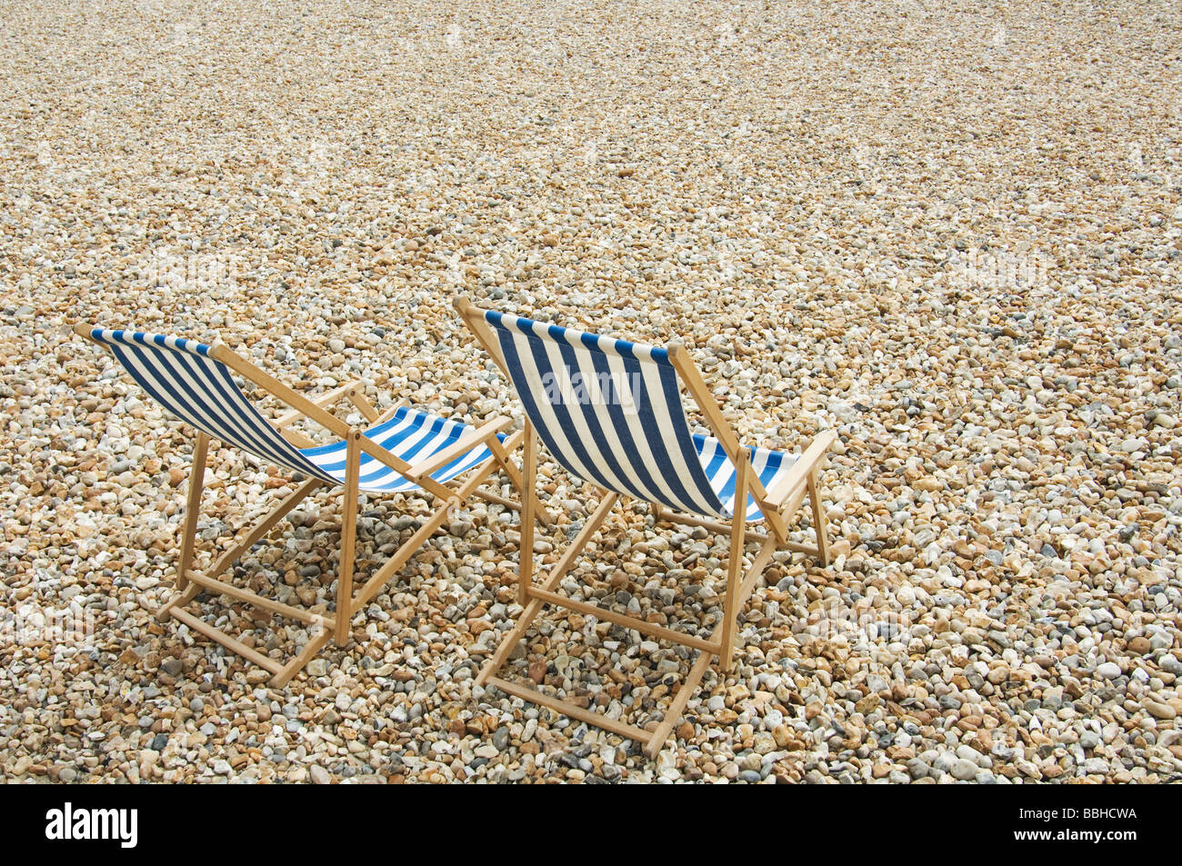 Two blue and white striped deck chairs on pebble beach Stock Photo