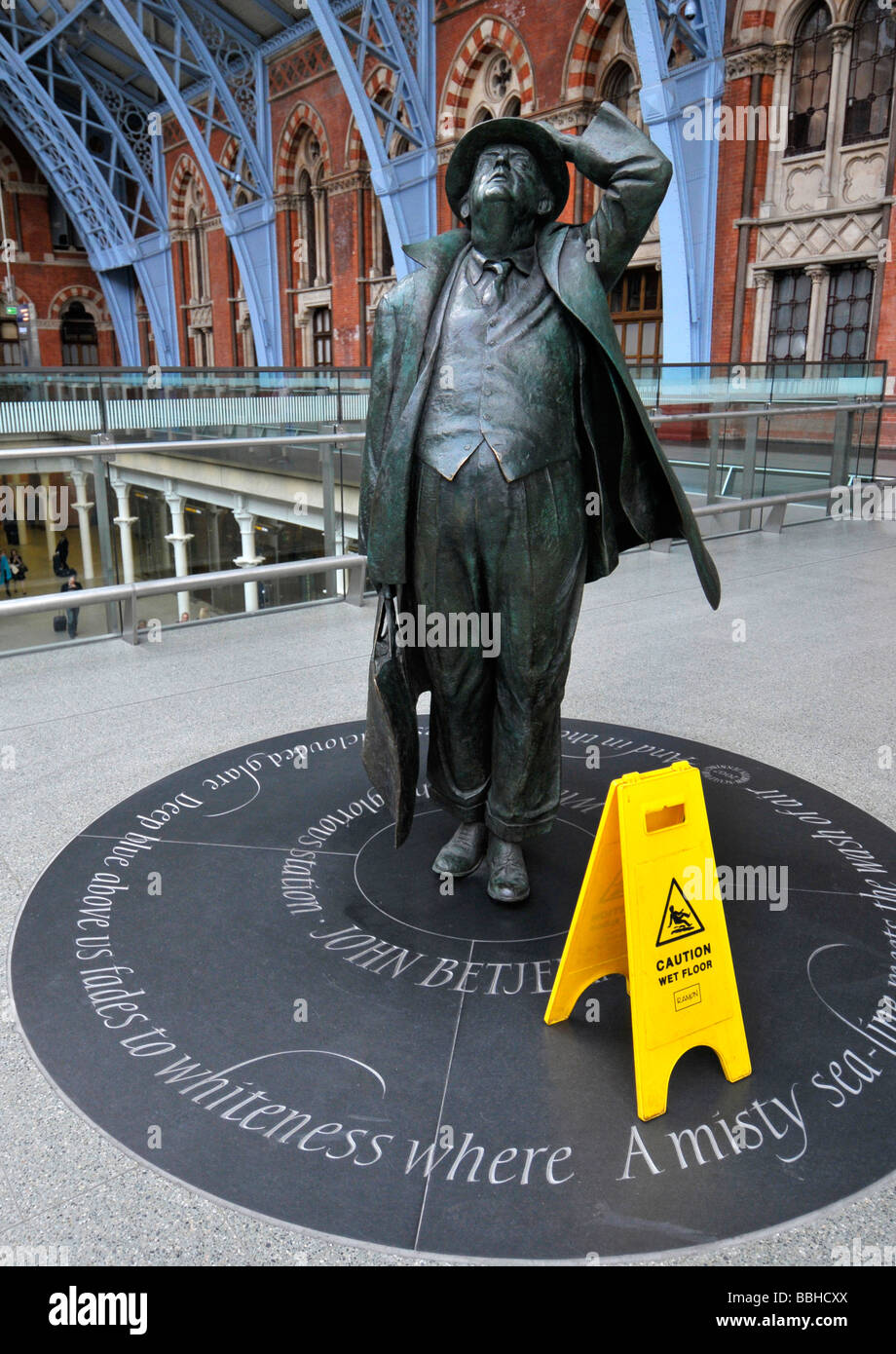 Statue of Sir John Betjeman with wet floor warning sign, St Pancras Train Station, London, Britain, UK Stock Photo