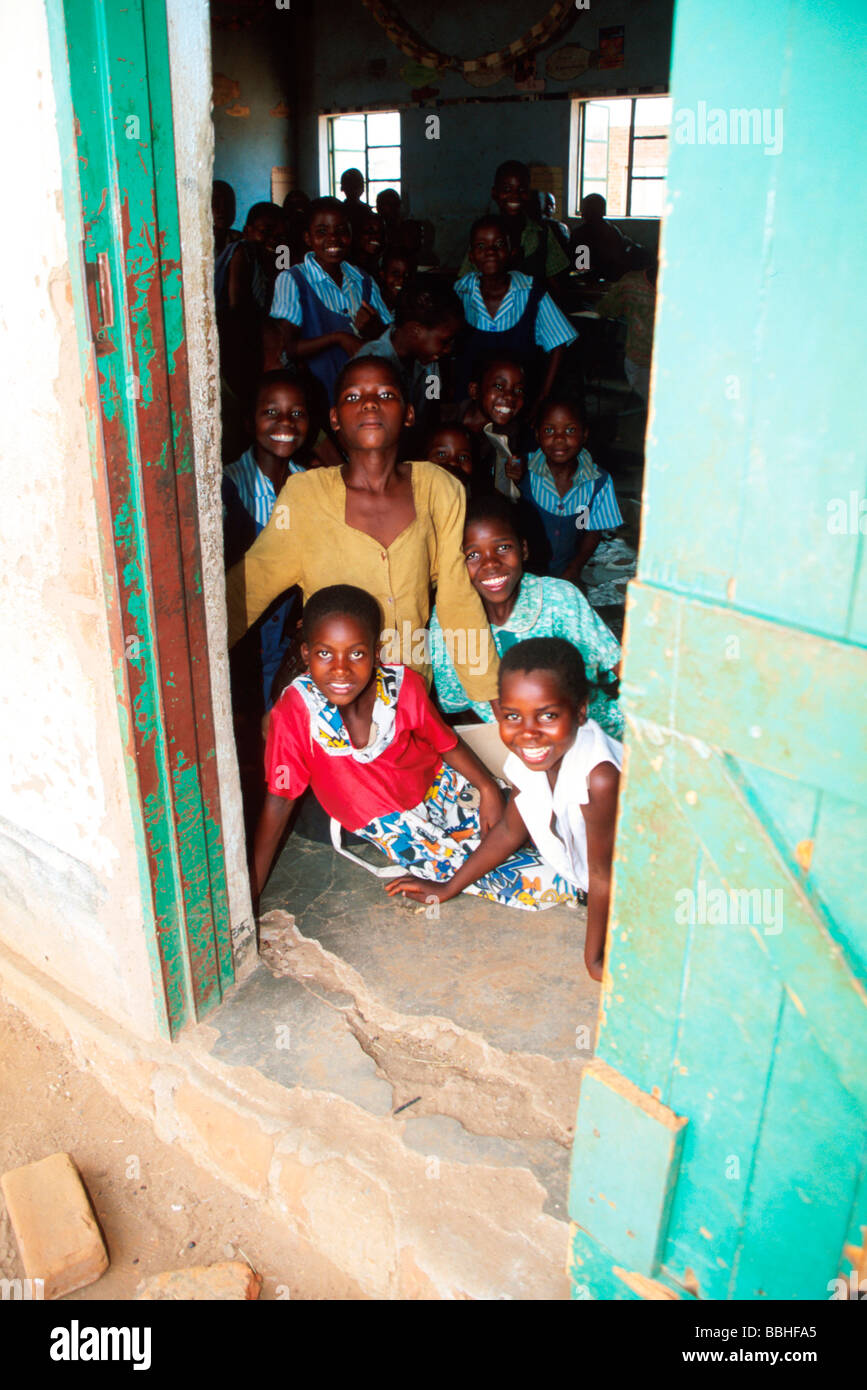 Faces still bright in spite of the hardships of life girls at Chimbuwe Primary School peer out of the shade of a classroom Stock Photo