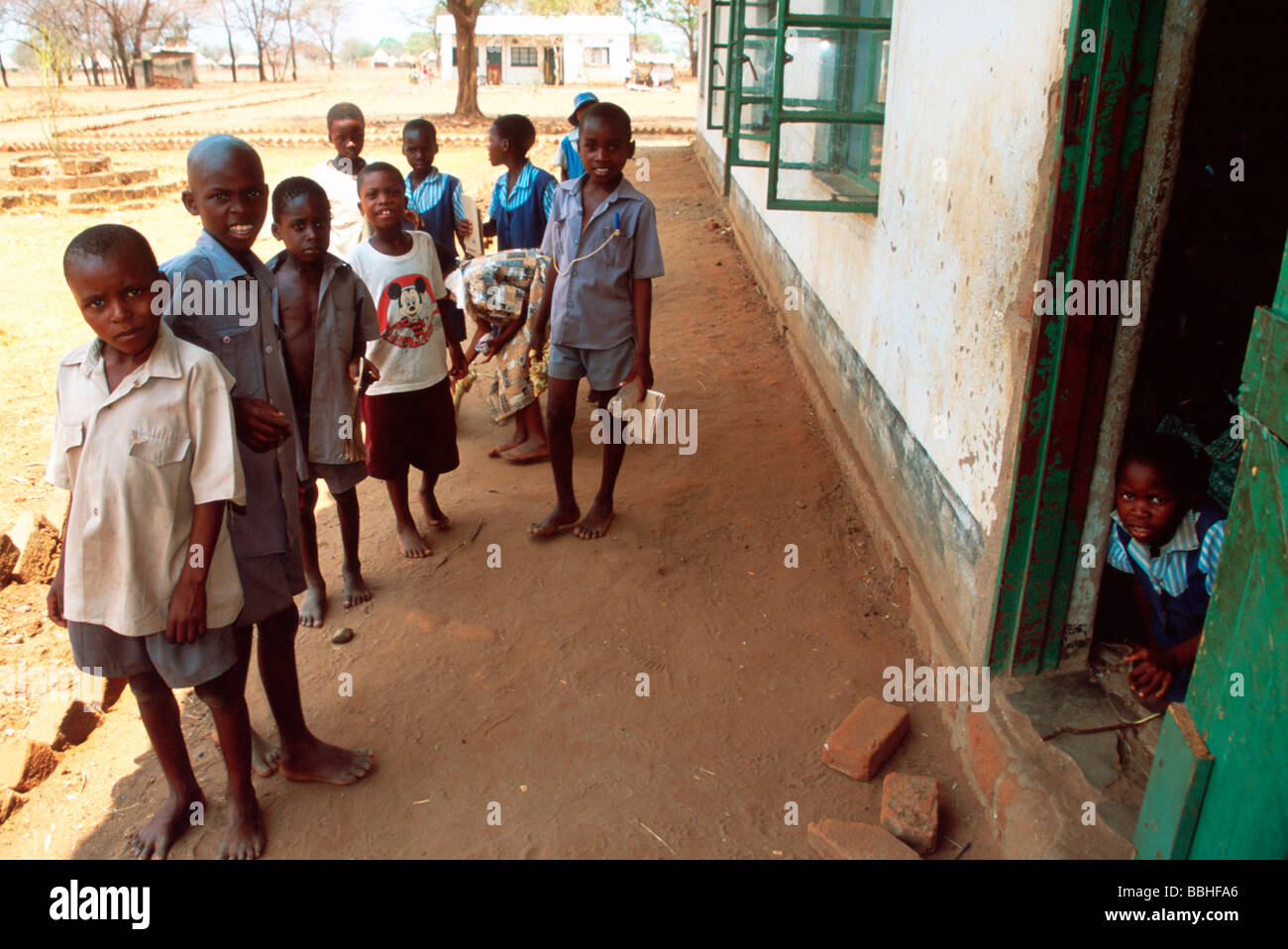 Faces still bright in spite of the hardships of life children at Chimbuwe Primary School stand in the shade outside their Stock Photo