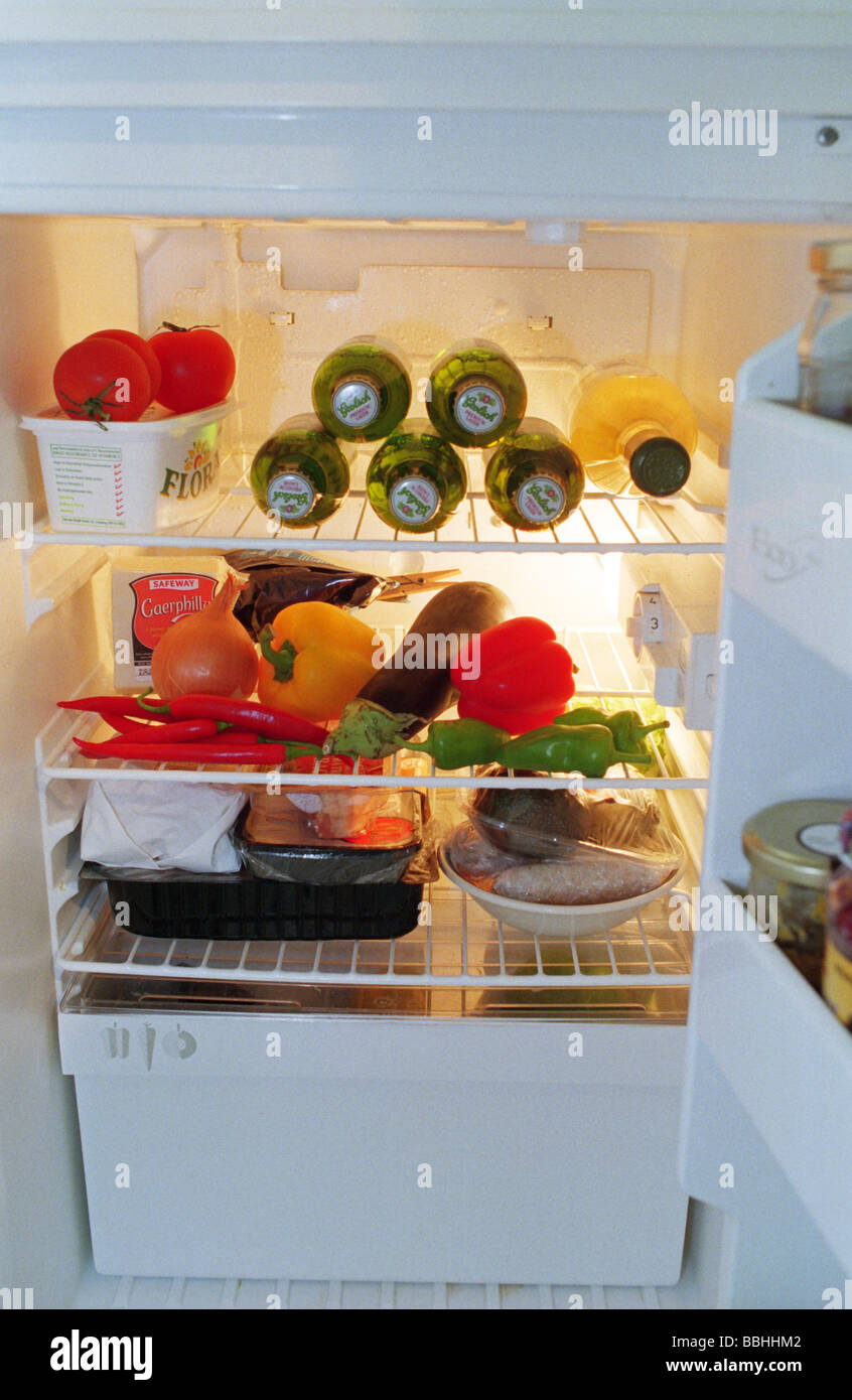 A fridge full of beer and vegetables, the refrigerator door open showing the contents inside. A open fridge full of food. Stock Photo