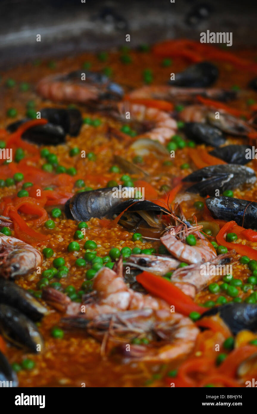 paella in large pan slowly cooking at a food fair. This spanish dish includes: chicken, peppers, rice, prawns and other seafood. Stock Photo