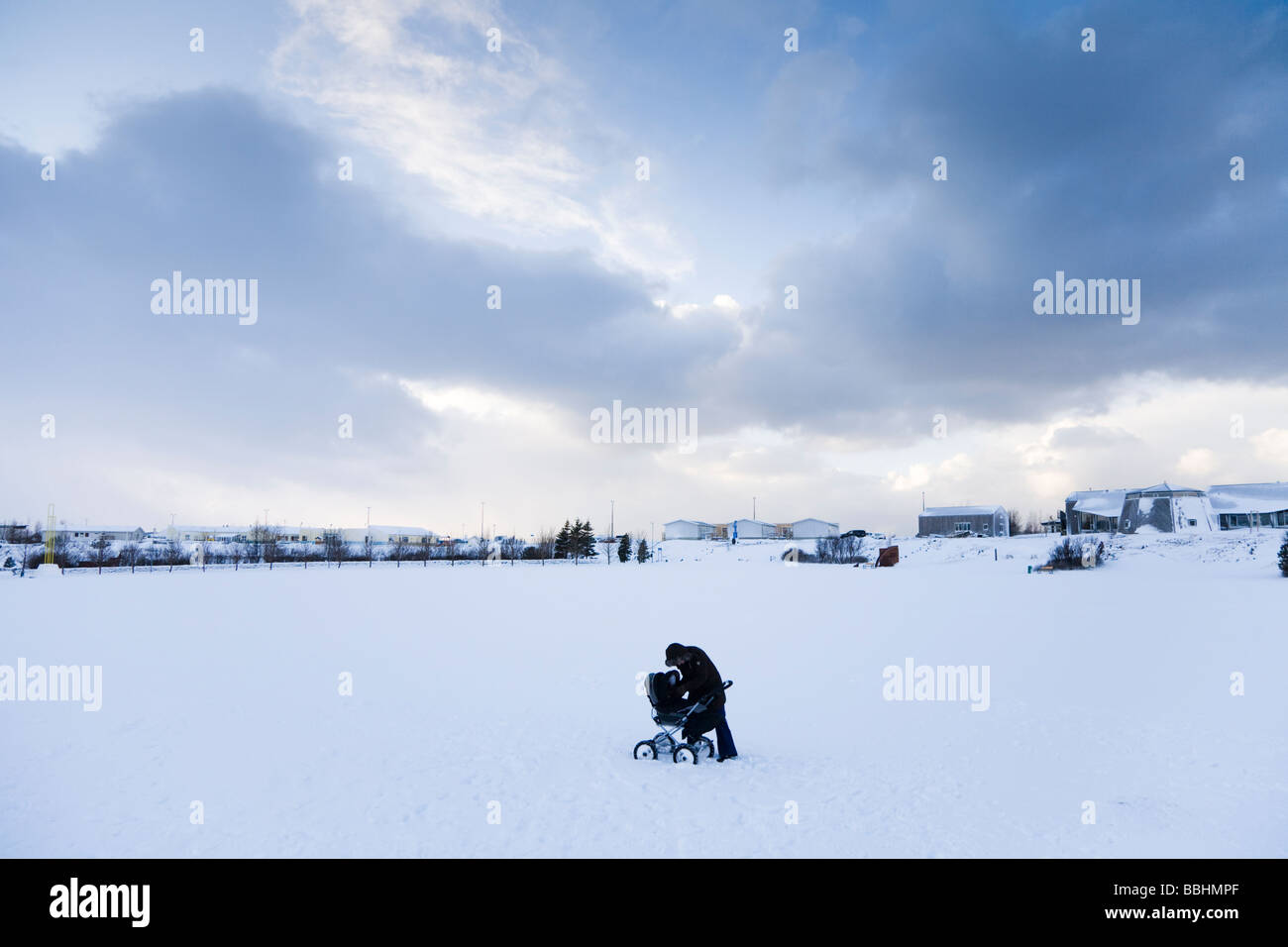 A woman caring for her baby in a pram in the snow. Hafnarfjordur, Greater Reykjavik Area, Iceland Stock Photo
