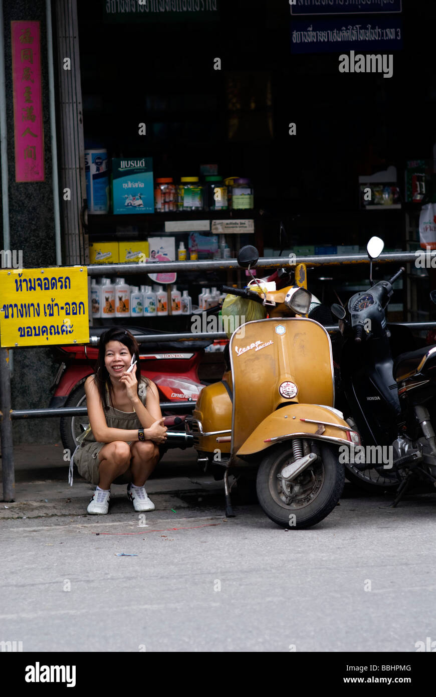 Woman crouching talking on a mobile phone next to a classic Vespa motorcycle Stock Photo