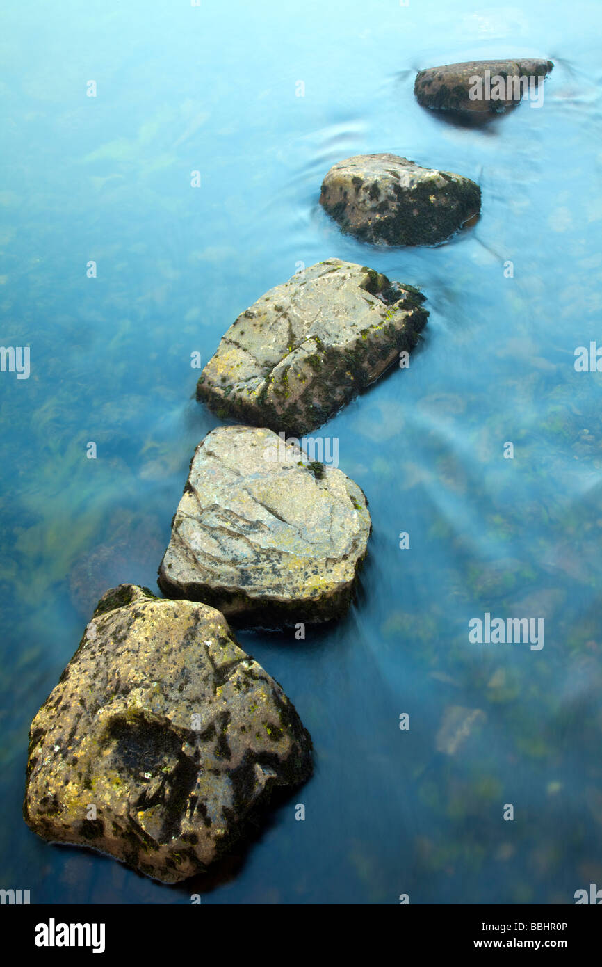 Five stepping stones in a small river in a diagonal row with the largest stone at the front of the row concept of leadership and direction Stock Photo