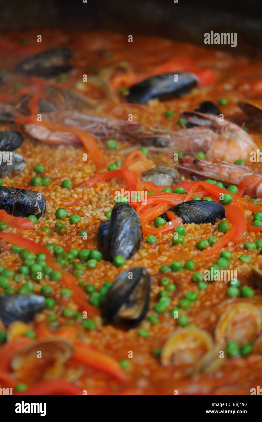 paella in large pan slowly cooking at a food fair. This spanish dish includes: chicken, peppers, rice, prawns and other seafood. Stock Photo