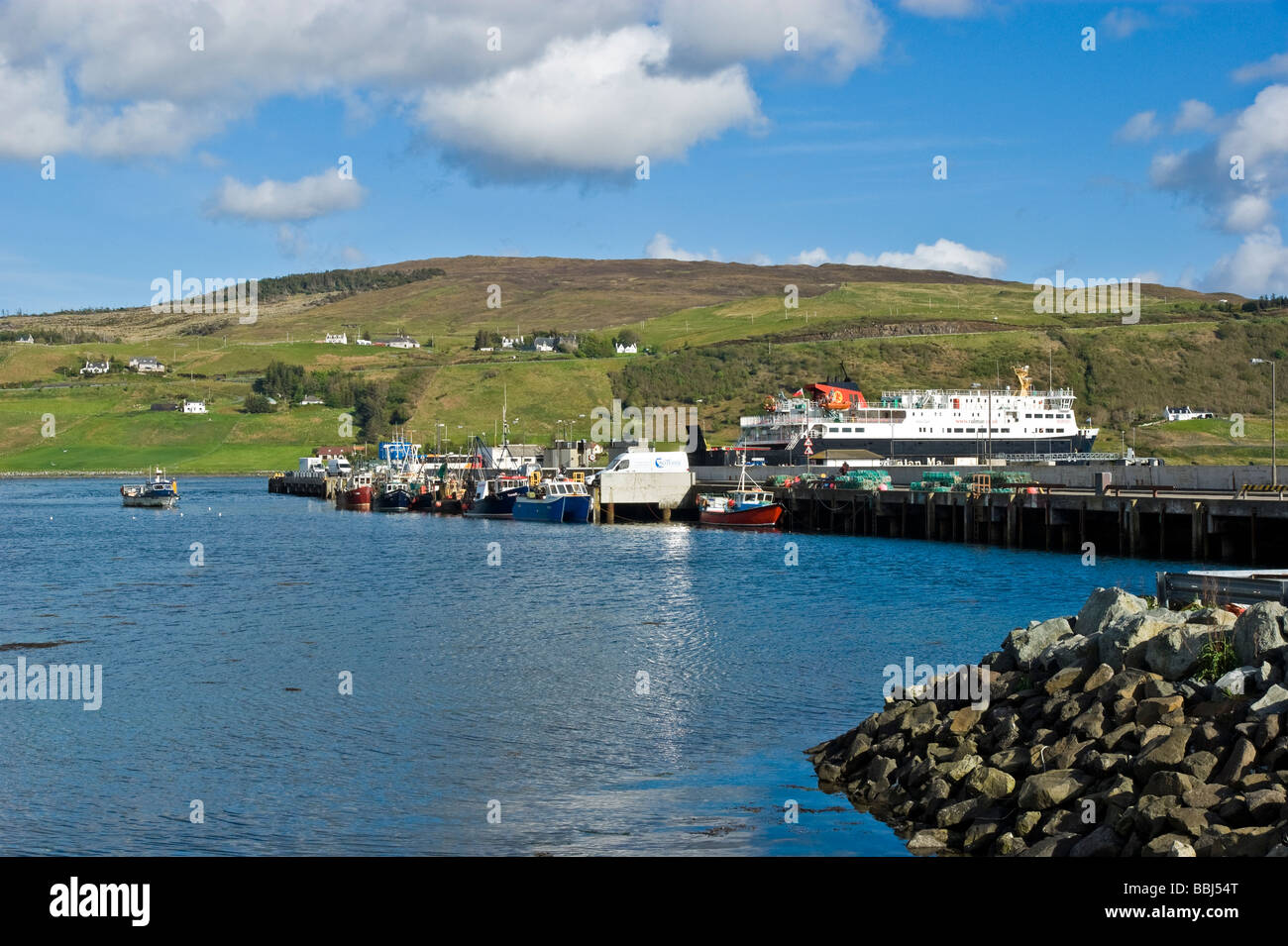 A fishing boat arrives at Uig harbour in Skye Scotland on a sunny spring day with the CalMac