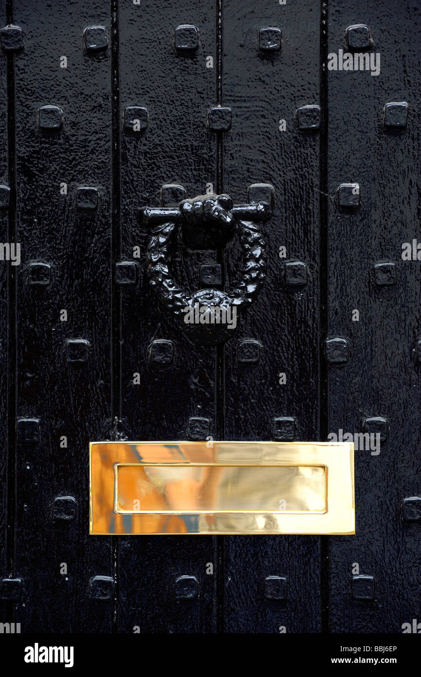 Black studded door with heavy knocker and shiny brass letterbox Stock Photo