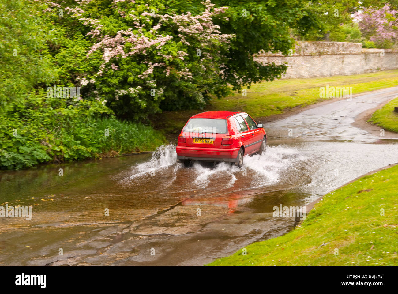 A car driving through a ford running across a country lane in the Uk countryside Stock Photo