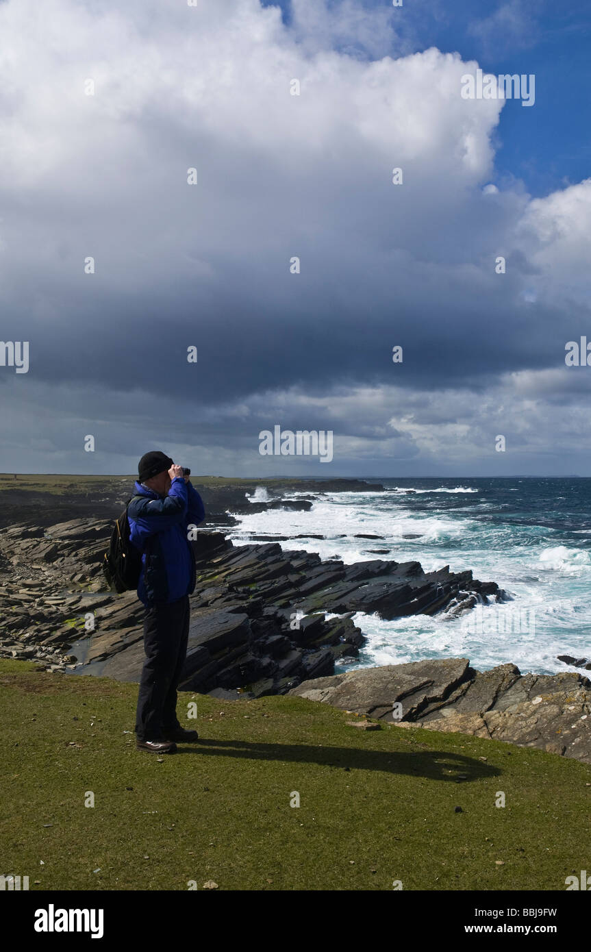 dh Bay of Ryasgeo NORTH RONALDSAY ORKNEY Birdwatcher looking out to sea and rocky coastline birdwatching binoculars Stock Photo