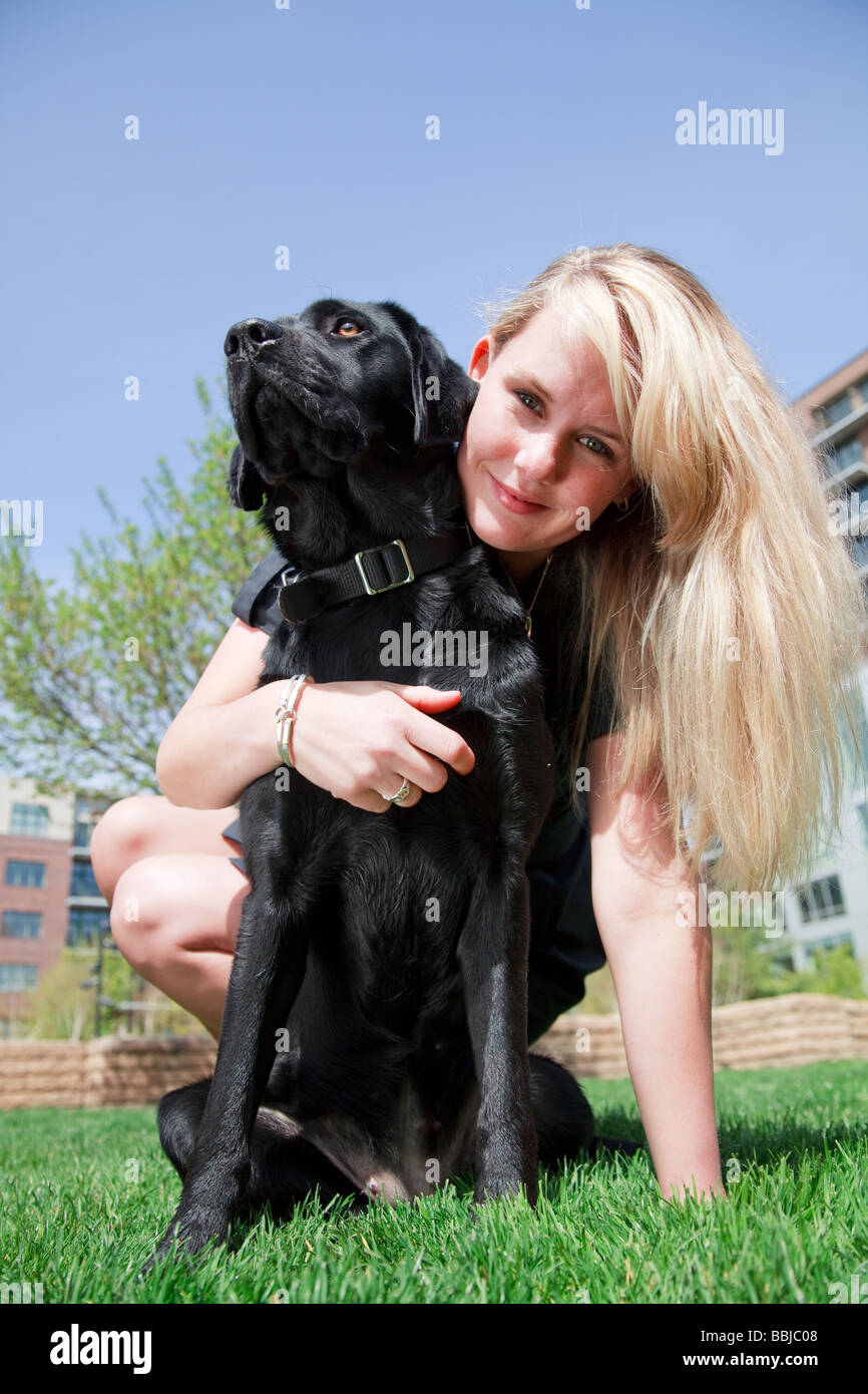 Blonde woman with her black labrador pet on green grass in outdoors ...