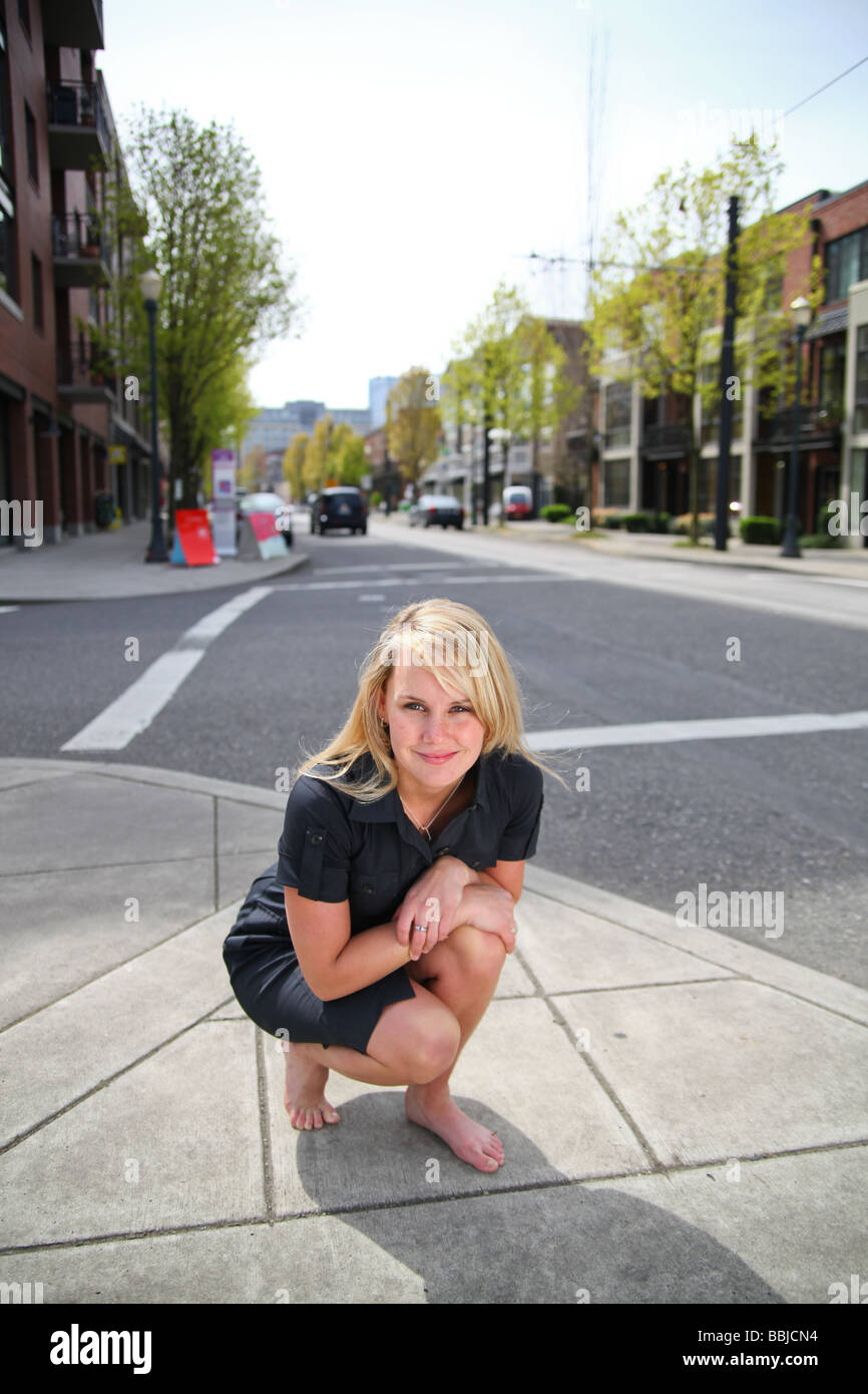 Cute blonde young woman crouching at street corner in urban condo environment. Stock Photo