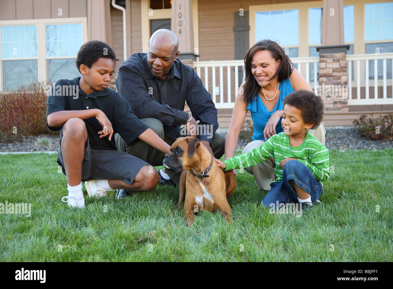 African American family petting dog in front of home Stock Photo