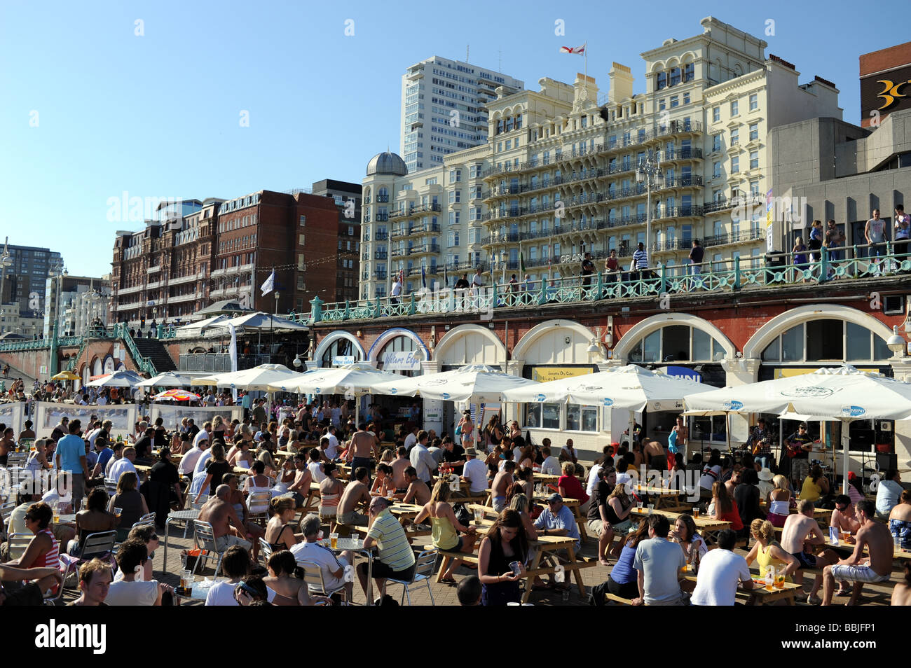 Crowds on Brighton beach and at the Gemini bar on the seafront UK with Grand Hotel in background Stock Photo