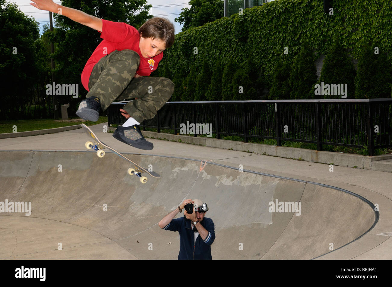 Young boy airborne on a skateboard above a concrete bowl at an outdoor Toronto Park with photographer Stock Photo