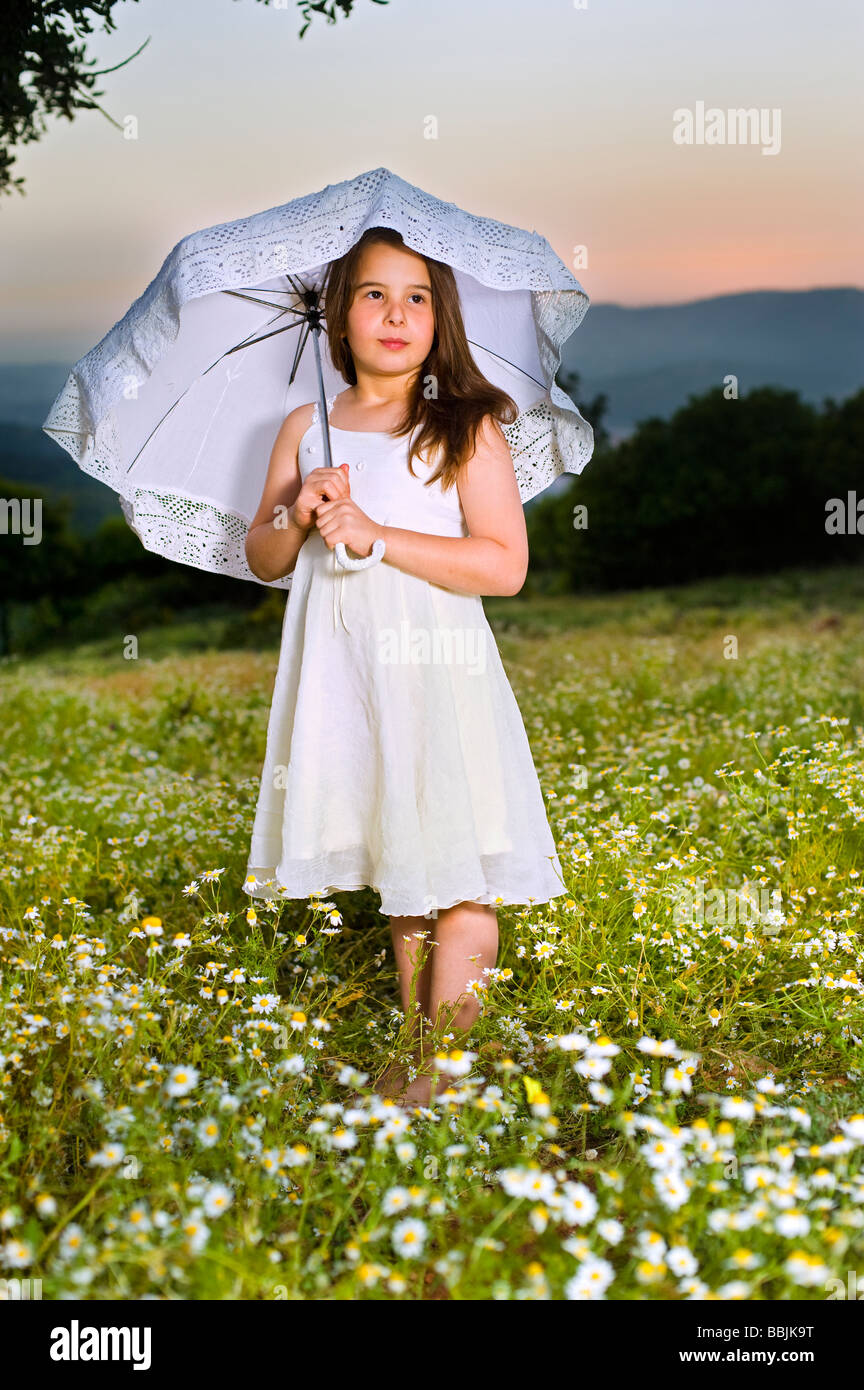 young girl in white dress with parasol in a flower field in sunset ...