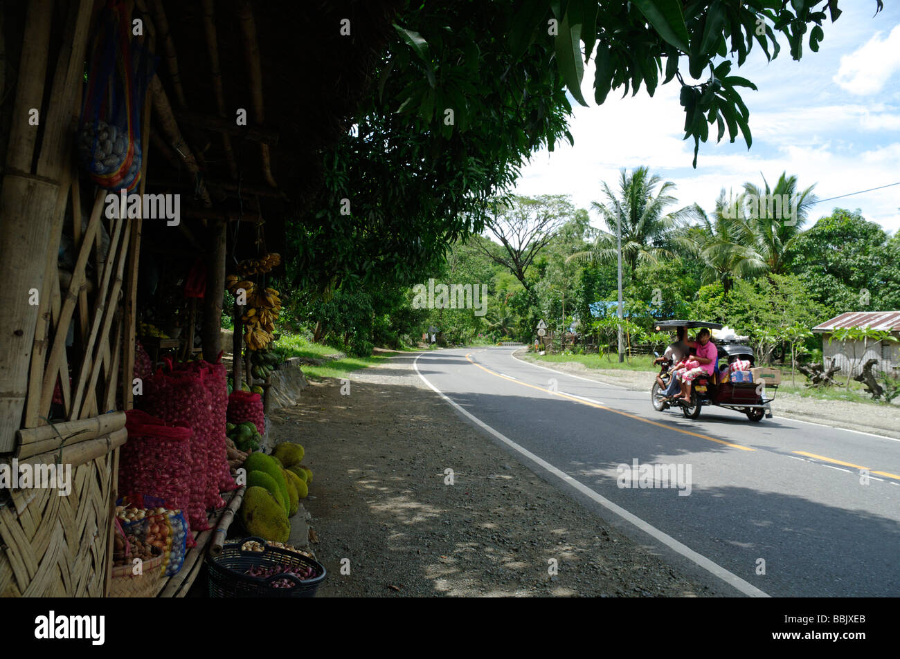 A tricycle passes a roadside fruit and vegetable stall, Nueva Ecija, North Luzon, Philippines Stock Photo