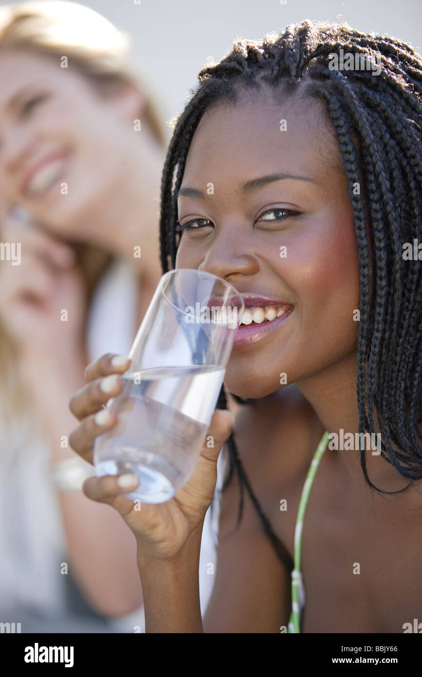Portrait of a young african woman with waterglass outdoors smiling at the camera, a female friend in the background out of focus Stock Photo