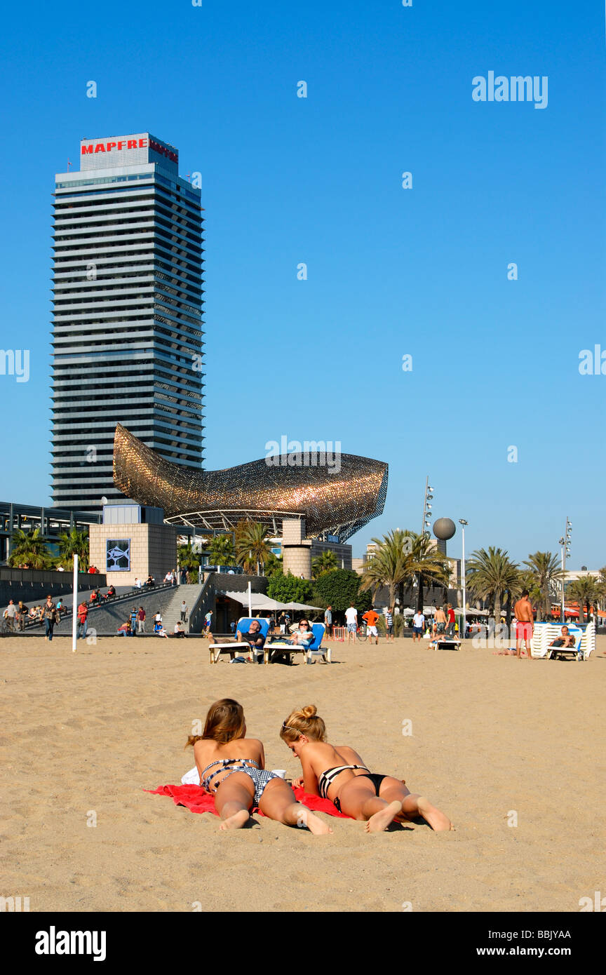 Sunbathers at Barceloneta Beach with Frank Gehry s Fish Peix Sculpture and Mapfre Tower Building Barcelona Catalonia Spain Stock Photo