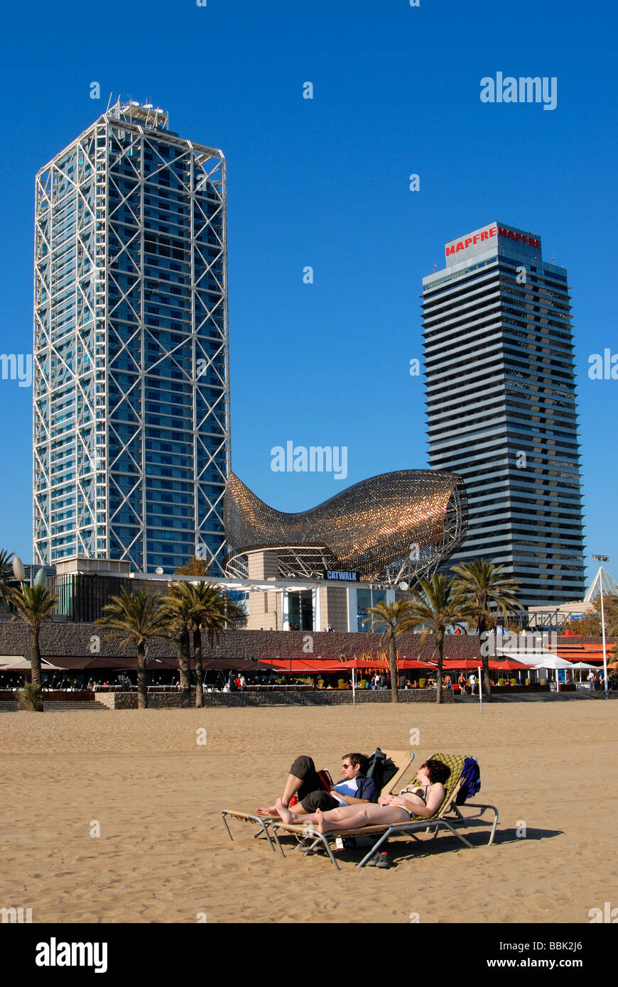 Sunbathers at Barceloneta Beach with Frank Gehry s Fish Peix Sculpture Mapfre Tower Building and Arts Hotel Barcelona Spain Stock Photo