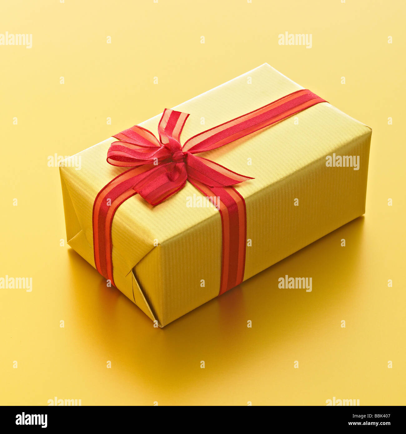 Luxury gold present with red ribbon on gold background. Stock Photo