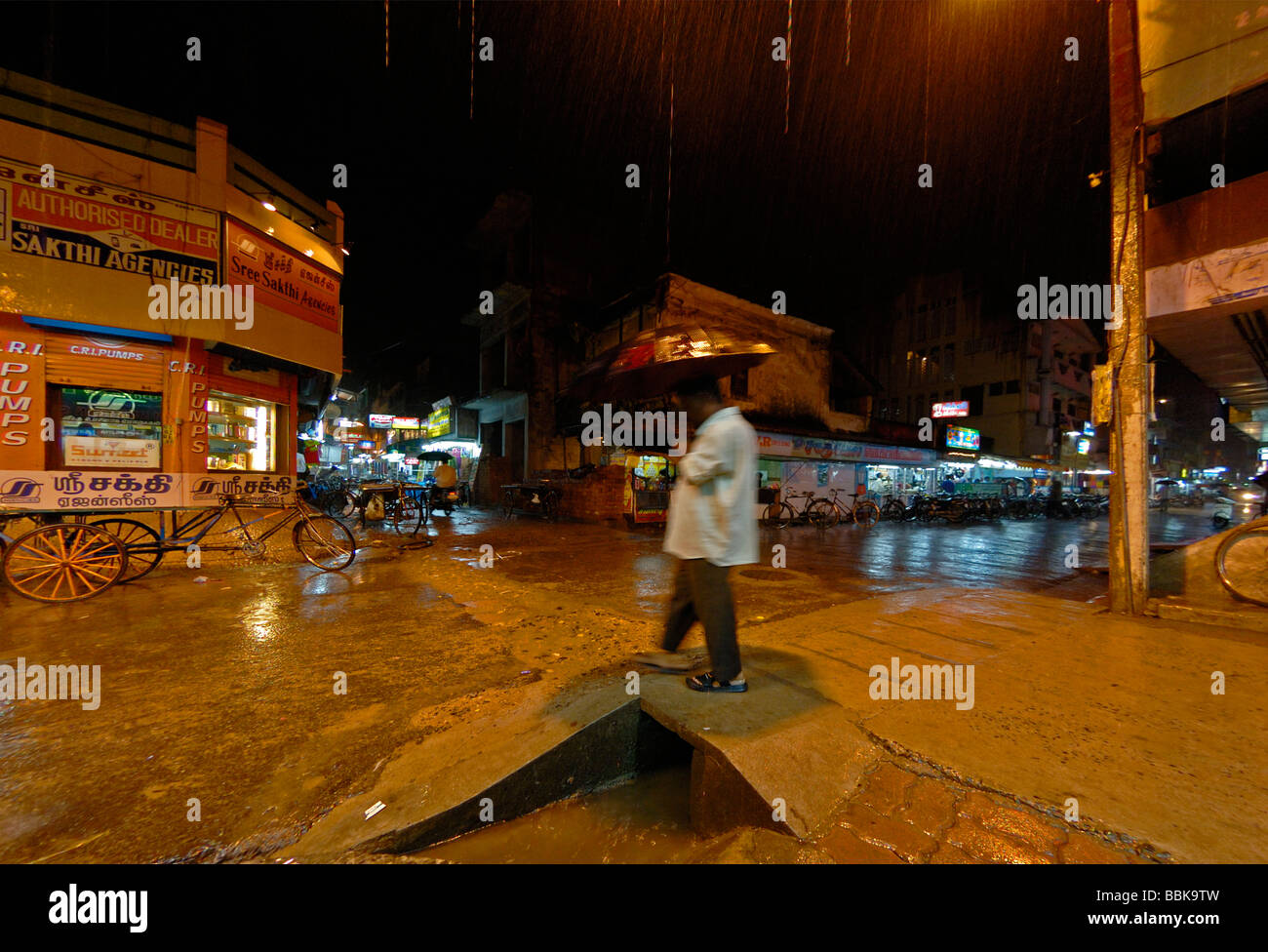 Indian man with umbrella crossing a road during heavy rain at nighttime in Pondicherry. India, Tamil Nadu, Pondicherry. Stock Photo
