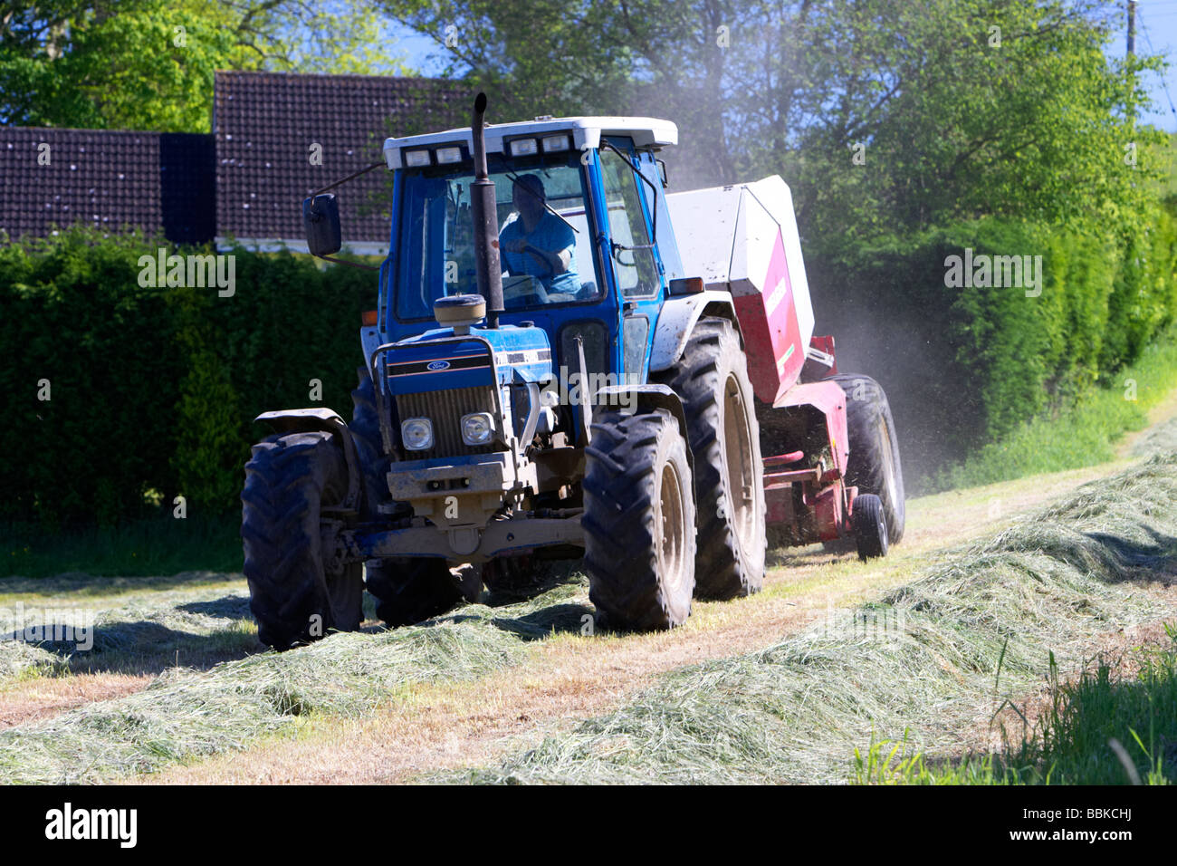 tractor towing baler collects grass cut for silage production county down northern ireland uk Stock Photo