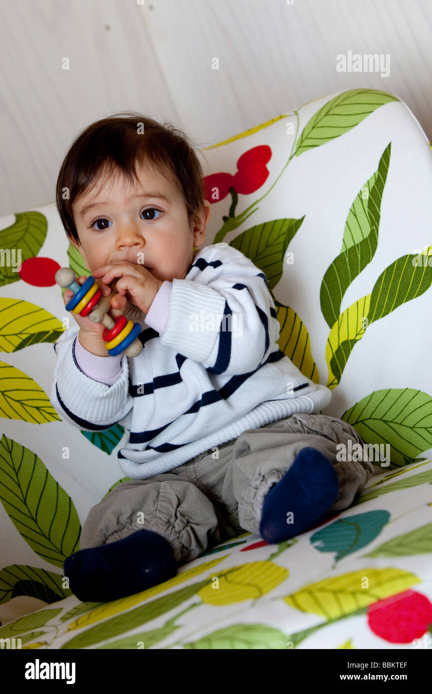 Nine-month-old baby sitting in a chair and biting into a rattle Stock Photo