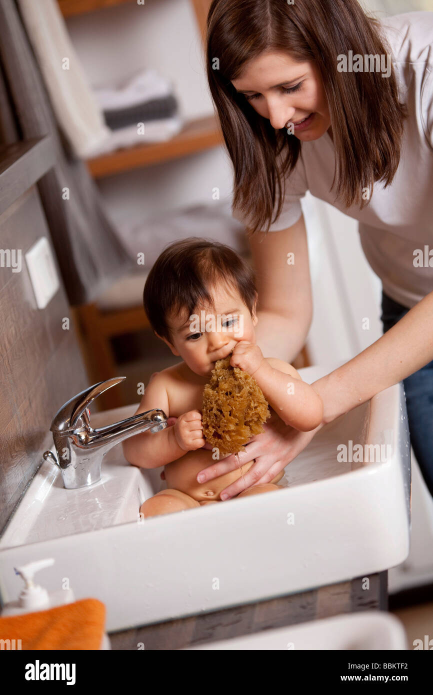 Nine-month-old baby is biting into a sponge while being bathed in the sink Stock Photo