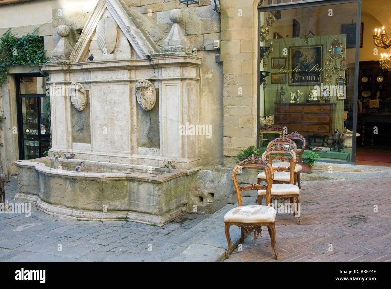 Antique chairs arrayed in the street outside the shop next to an ancient wash fountain in Corso Italia Arezzo Stock Photo