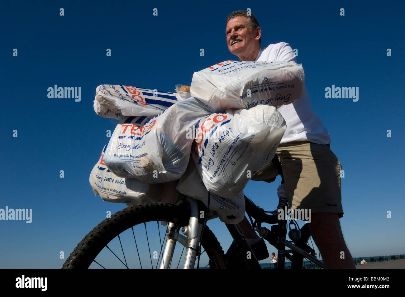 A man coming back from shopping at Tesco on a bike with laden with plastic bags full of groceries. Stock Photo