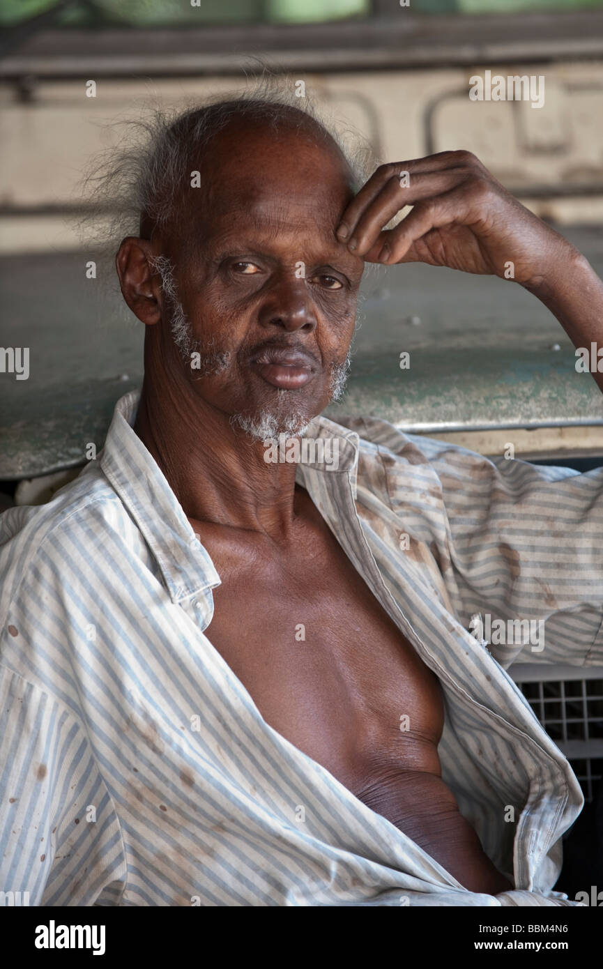An old man leaning back against an ancient vehicle at Douglas Plantation in Grenada Stock Photo