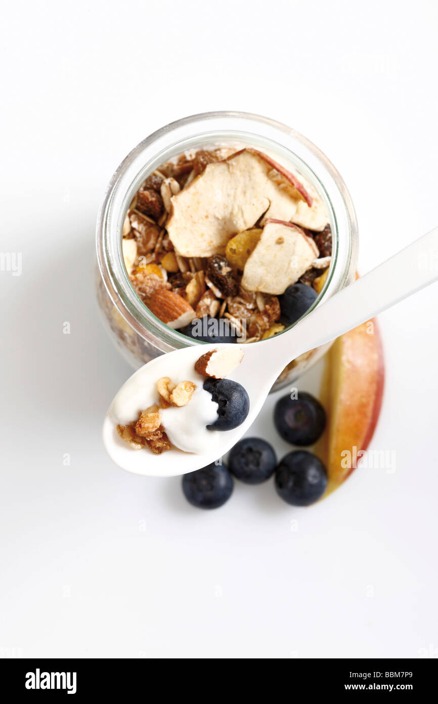 Muesli with yoghurt in a small glass jar, yoghurt spoon, blueberries, dried fruit, apple Stock Photo
