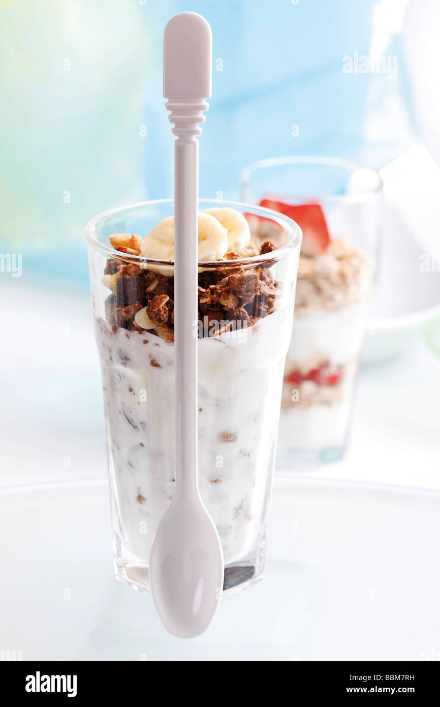 Chocolate muesli with yoghurt in a small glass jar, sliced banana, yoghurt spoon and strawberry muesli Stock Photo