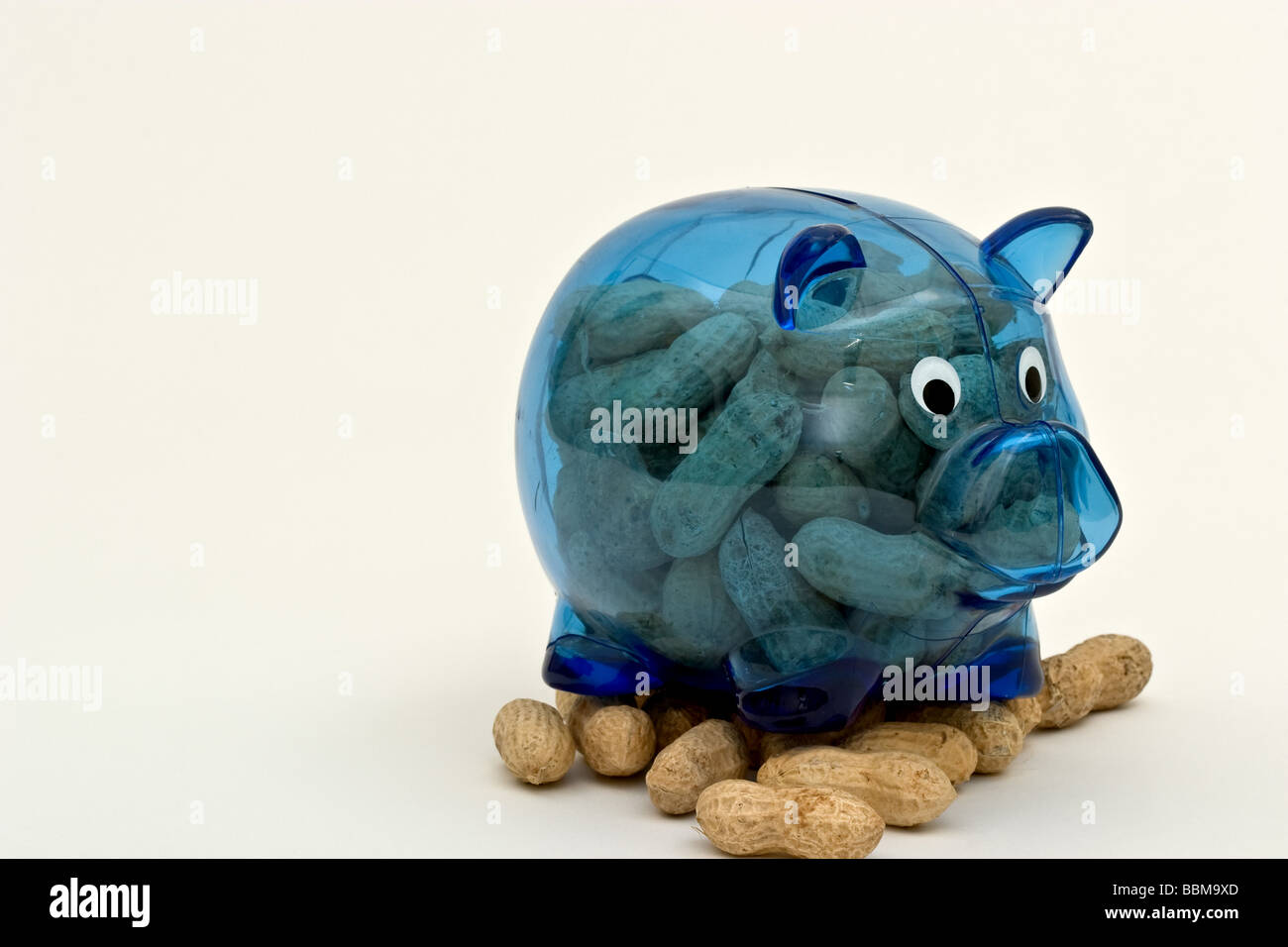 Clear blue piggy bank filled with and sitting on unshelled peanuts Stock Photo