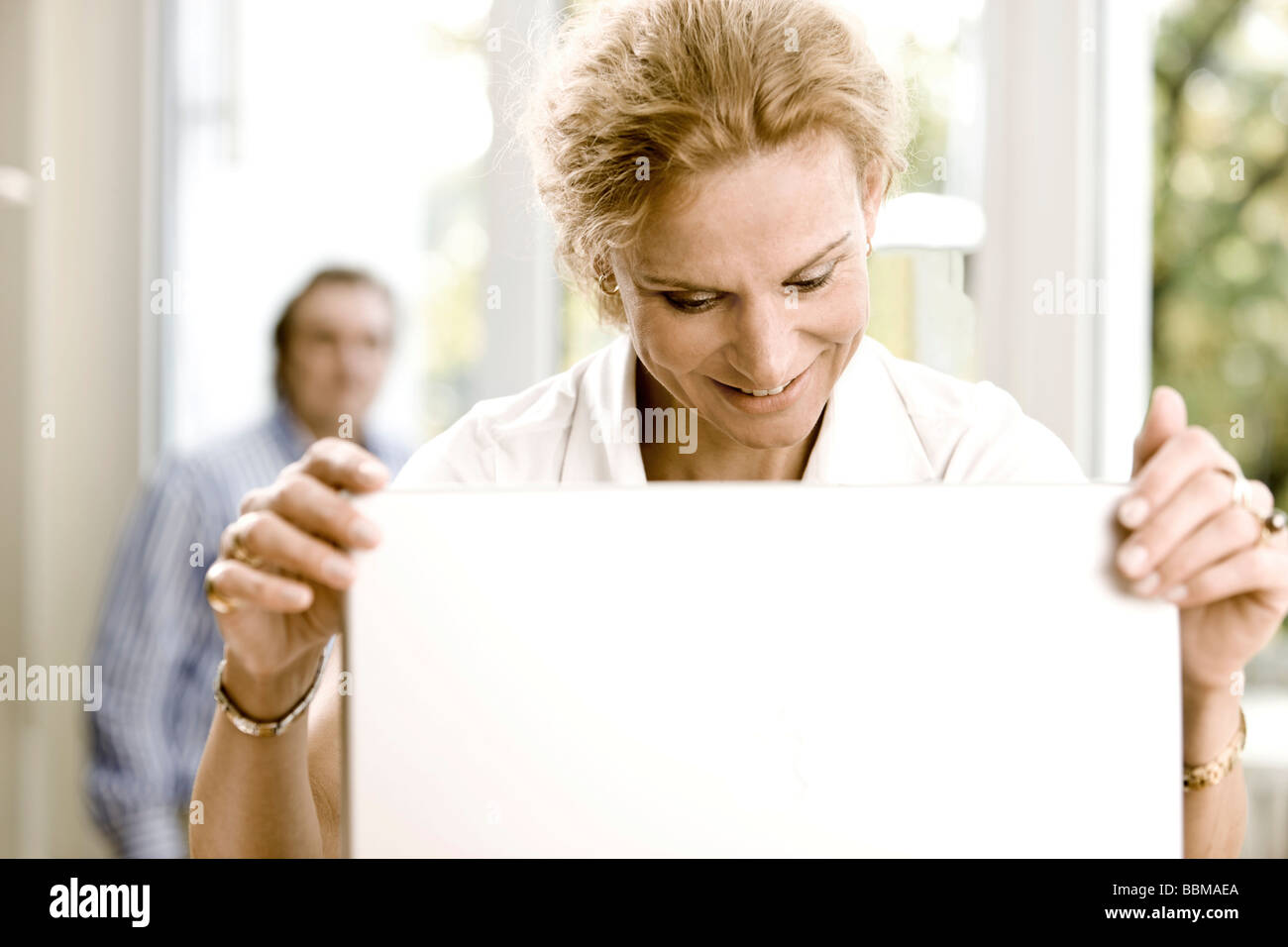 Woman working on a laptop, man in the back Stock Photo