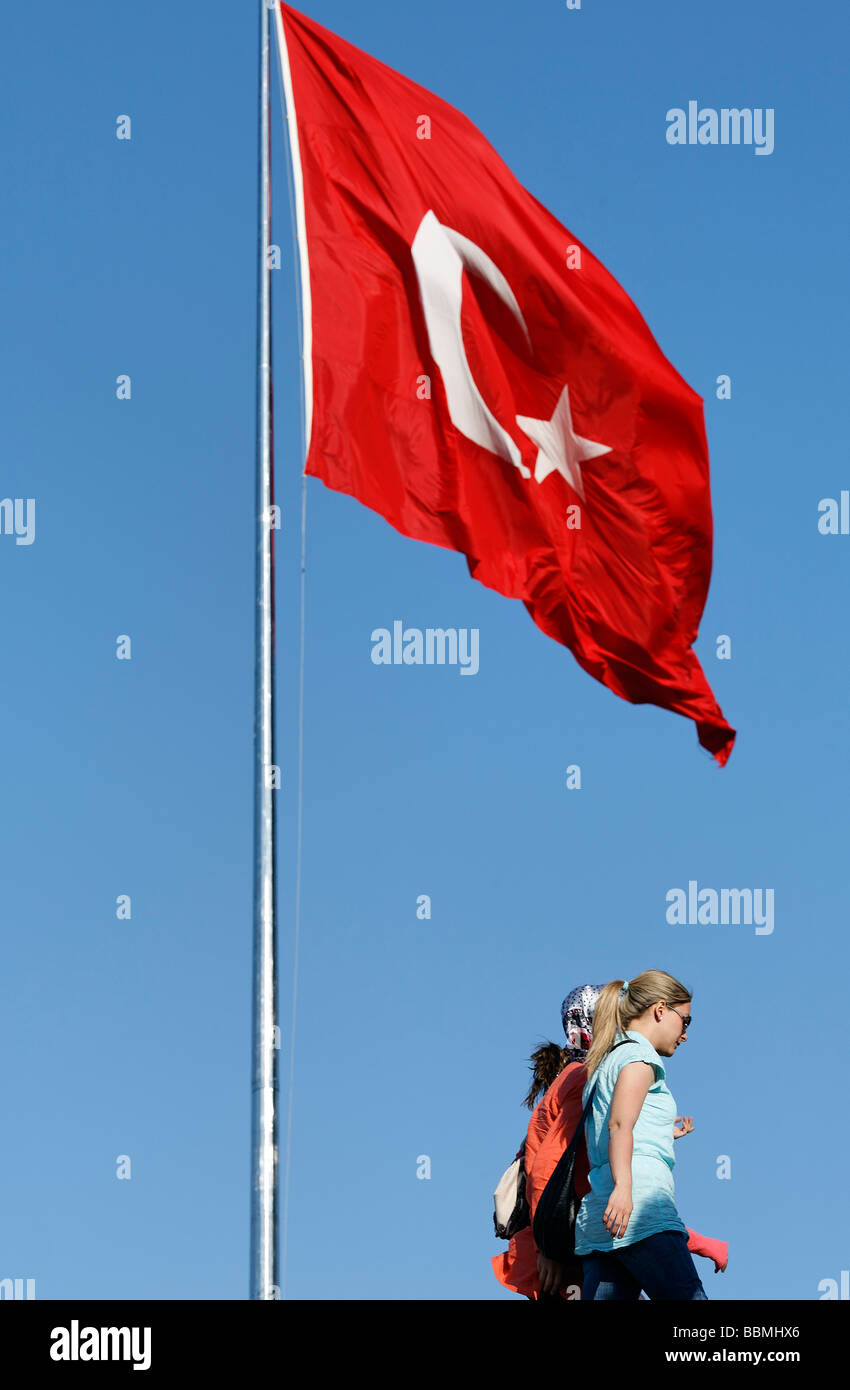 Young women in European clothes walking under the Turkish flag, Taksim Square, Beyoglu, Istanbul, Turkey Stock Photo
